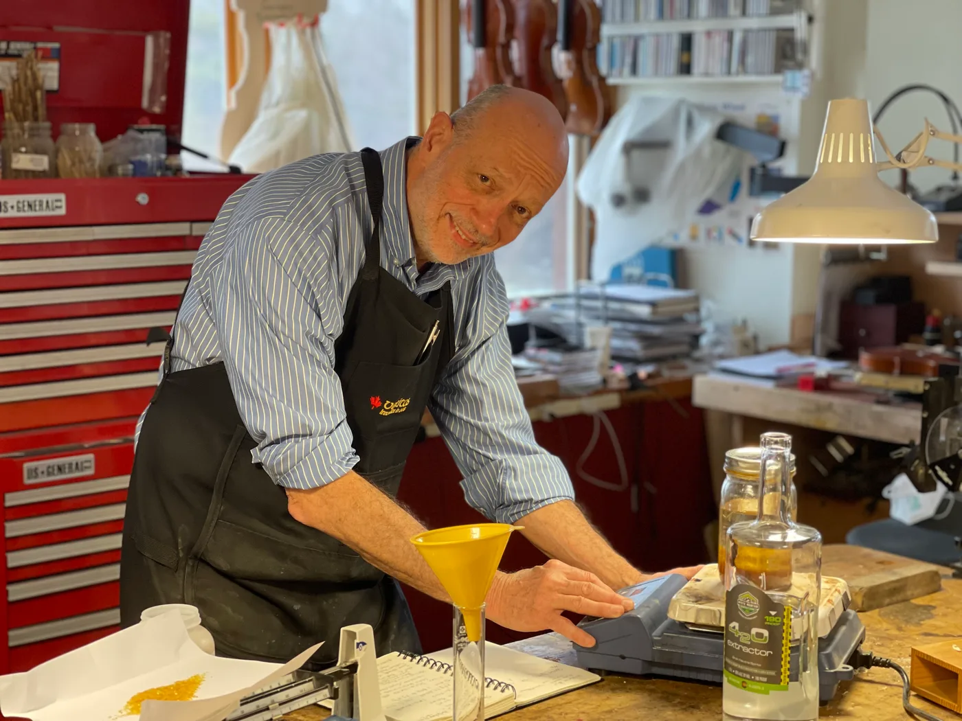 Kevin Flannery at his bench applying finish to an instrument, smiling.