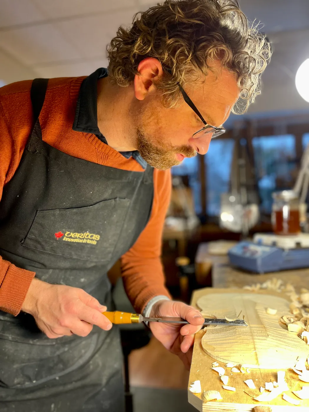 Matthew Noykos carving a violin top plate with a chisel, wood shavings on the bench.